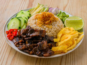 Assiette de riz avec porc caramélisé, omelette, concombre, citron vert, piments rouges et légumes frais.