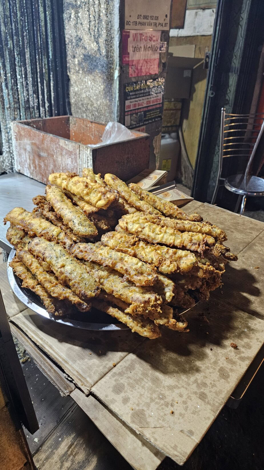 Assiette de beignets frits empilés sur une table en carton dans un environnement de rue.
