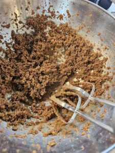 Mélange brun de pâte à gâteau dans un bol en métal avec des fouets électriques.