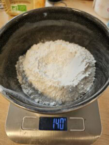 Bol de farine pesé à 140 grammes sur une balance de cuisine électronique.