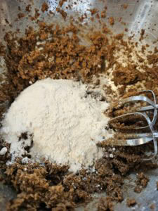 Mélange de pâte à biscuits avec de la farine ajoutée dans un bol en métal, prêt à être mélangé avec un batteur électrique.