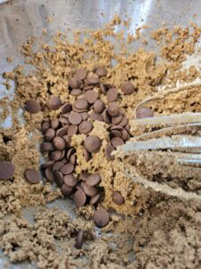 Pâte à cookies avec des pépites de chocolat dans un bol en métal, prête à être mélangée.