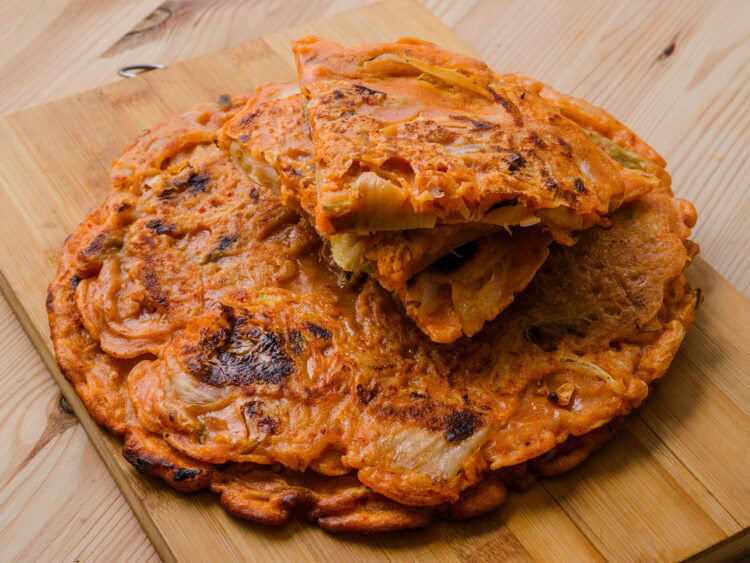 Galette coréenne au kimchi coupée en parts, servie sur une planche en bois.