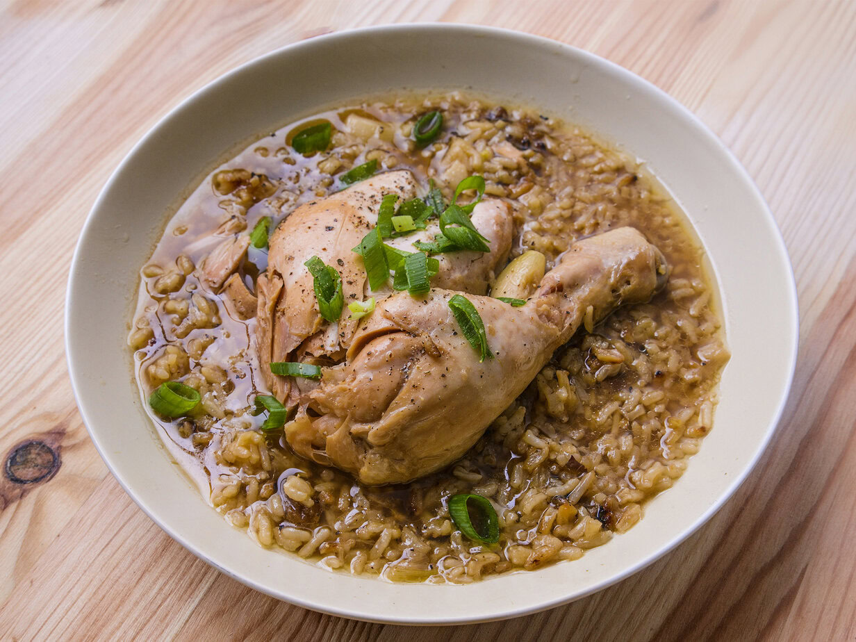 Poulet mijoté avec riz et sauce, garni d’oignons verts, servi dans une assiette blanche sur une table en bois.