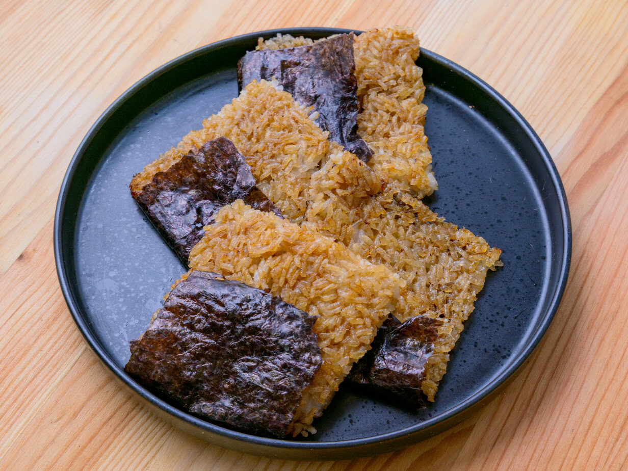 Assiette de galettes de riz gluant grillées enveloppées partiellement de feuilles de nori, sur une table en bois.