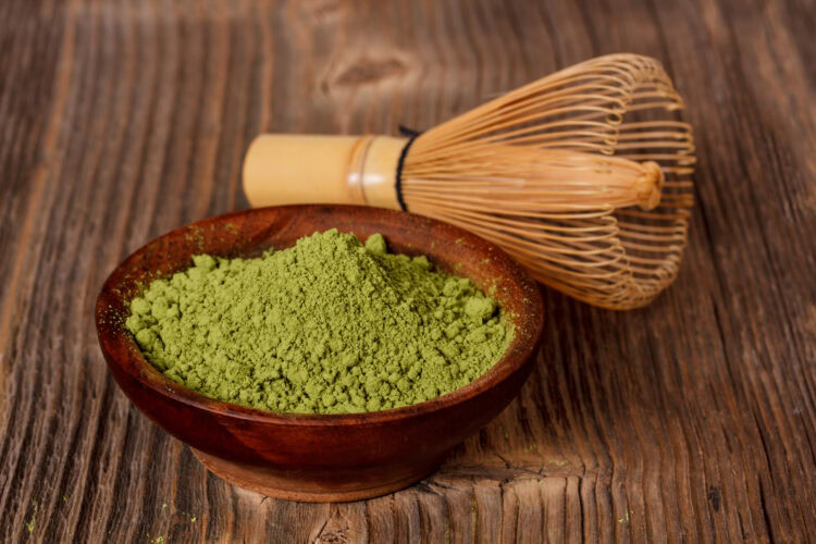 Bol de poudre de matcha verte avec un fouet en bambou sur une table en bois.