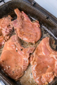 Côtelettes de porc en train de cuire dans une poêle avec du jus et des épices.