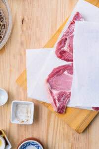 Deux côtelettes de porc crues sur une planche, épongées avec du papier absorbant.