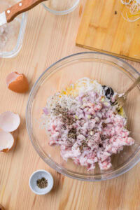 Ingrédients pour farce (viande, vermicelles, œuf, échalote, poivre) dans un saladier sur une table en bois.