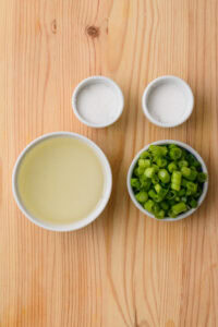 Quatre bols contenant du sel, du sucre, de l’huile et des oignons verts tranchés sur une table en bois.