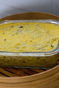 Plat de flan salé aux vermicelles dans un plat en verre, posé sur un panier vapeur en bambou.