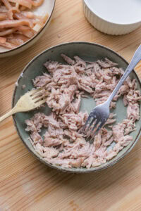 Poulet effiloché dans une assiette verte avec deux fourchettes, sur une table en bois.