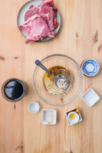 Côtelettes de porc crues et ingrédients pour marinade disposés sur une table en bois.
