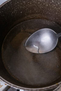 Cuillère en métal dans une casserole contenant un liquide transparent, probablement du sirop de sucre.