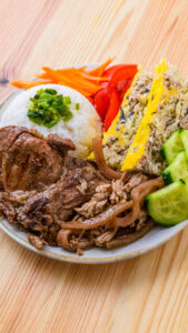 Assiette de riz, porc grillé, pâté vietnamien, légumes frais et crudités sur une table en bois.