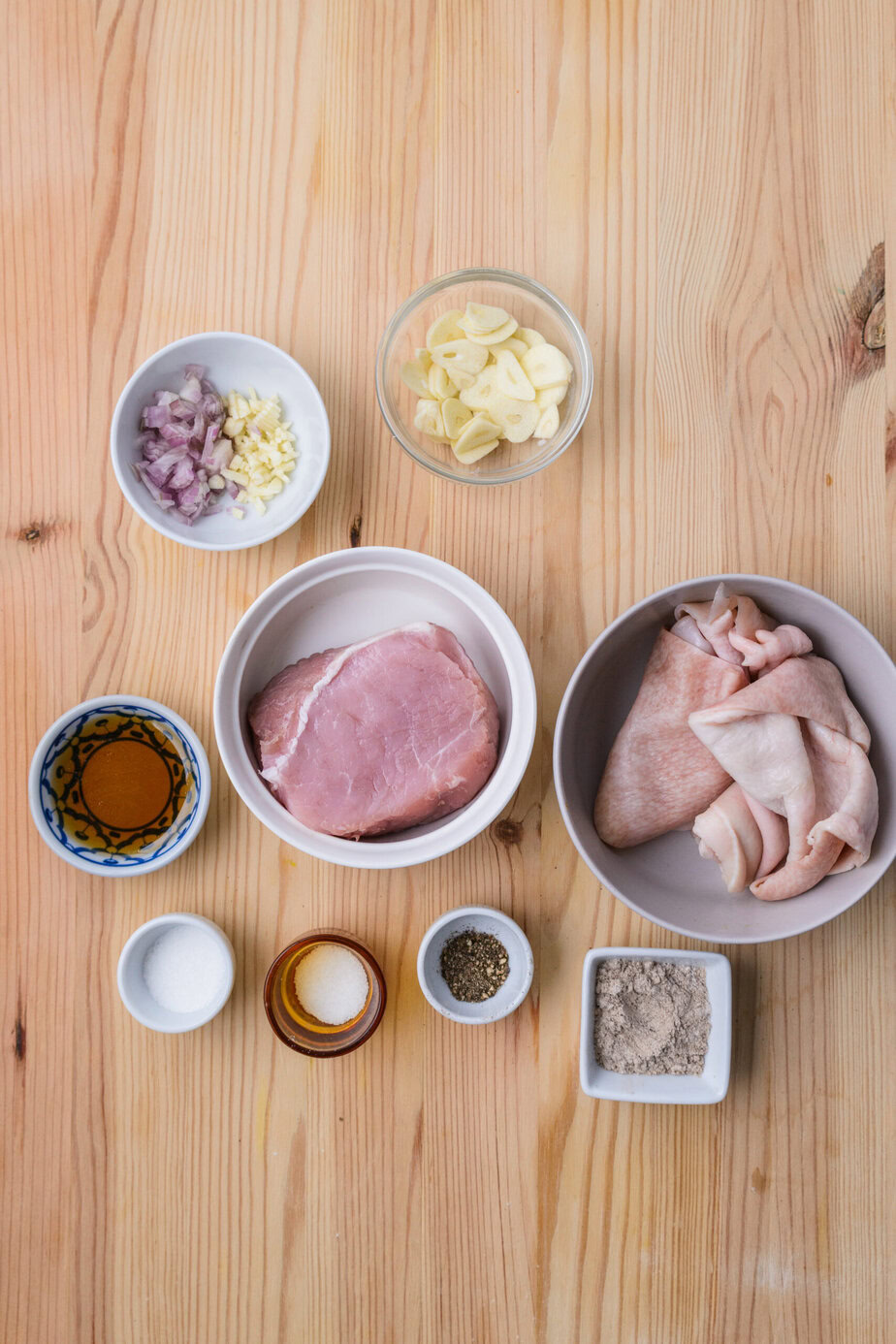 Ingrédients sur une table : viande de porc, couenne, ail, échalote, épices, sel, sucre, sauce et poudre.