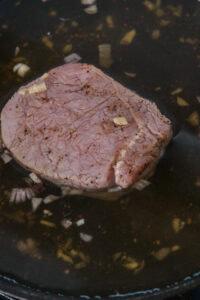 Tranche de viande crue dans une marinade avec morceaux d’ail et d’oignon.