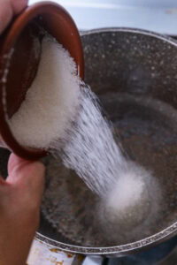 Du sucre est versé d’un bol dans une casserole.