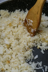 Tapsilog - Ajouter le riz froid et le défaire à la spatule, puis le faire sauter jusqu’à ce qu’il soit bien chaud et que les grains se séparent.