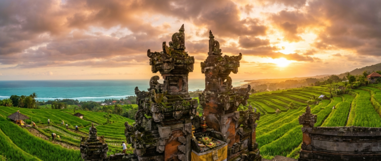 Temple balinais devant des rizières en terrasses au coucher du soleil, avec vue sur l’océan.