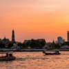 Bateaux sur une rivière devant le Wat Arun à Bangkok au coucher du soleil.