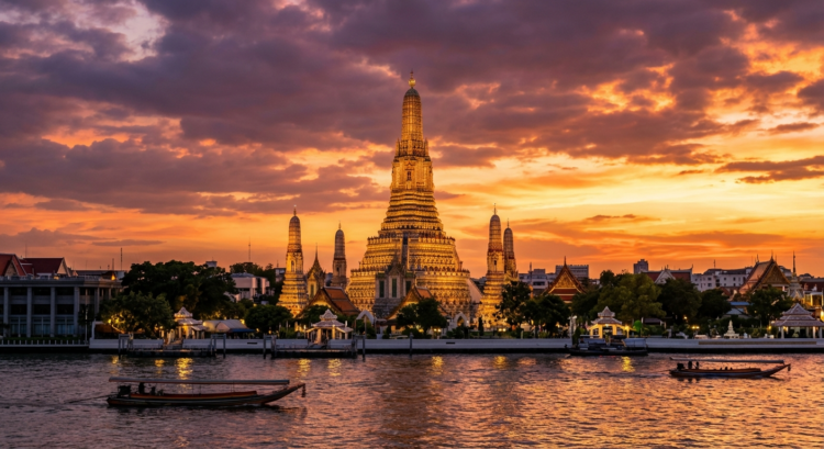 Temple illuminé au bord d'une rivière au coucher du soleil, avec des bateaux sur l'eau.