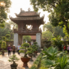 Temple asiatique traditionnel entouré de jardins, avec des visiteurs marchant sur une allée pavée.