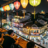 Terrasse animée avec lanternes colorées surplombant une rue animée de nuit dans une ville asiatique.