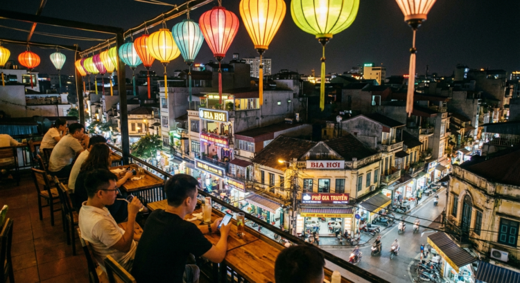 Terrasse animée avec lanternes colorées surplombant une rue animée de nuit dans une ville asiatique.