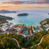 Vue aérienne d’une station balnéaire entourée de collines verdoyantes et d’une mer turquoise au coucher du soleil.