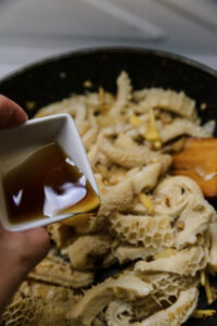 Une main verse une sauce brune sur des tripes en cuisson dans une poêle.