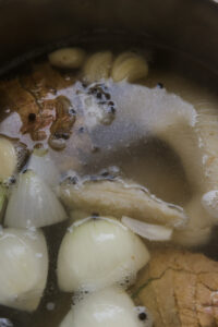 Bouillon en cuisson avec oignons, ail, poivre, laurier et viande dans une casserole.