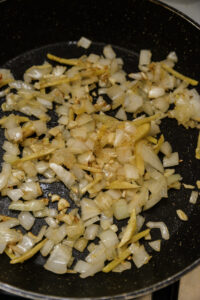 Oignons et ail émincés en train de revenir dans une poêle noire.