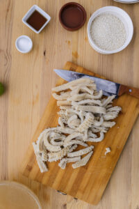 Tripes coupées sur une planche en bois avec un couteau, riz et condiments autour.