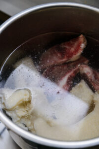 Morceaux de viande et de gras dans une marmite d'eau en train de bouillir.