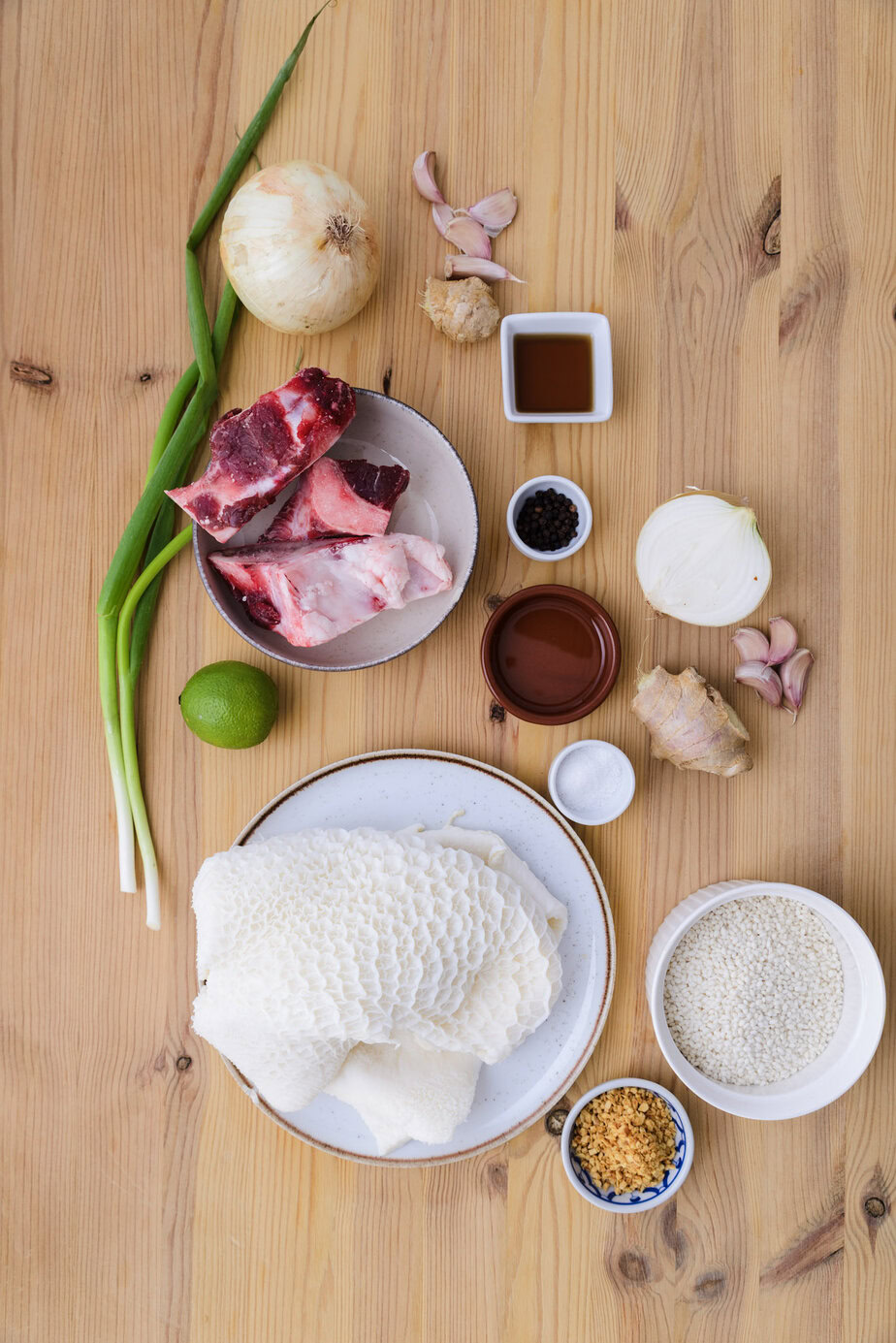 Ingrédients variés sur une table en bois : tripes, os à moelle, riz, oignon, ail, gingembre, citron vert et condiments.