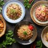 Cinq assiettes de riz sauté varié, garnies de crevettes, œuf, légumes et herbes, sur une table en bois.
