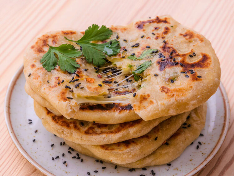 Galettes naan au fromage, garnies de coriandre fraîche et de graines de sésame, servies sur une assiette.