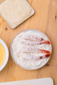 Ebi fry - Recette authentique - Paner: Tenir chaque crevette par la queue, l'enrober uniformément du mélange de farine, puis tapoter pour enlever l'excédent, en insistant dans les rainures et zones décollées.