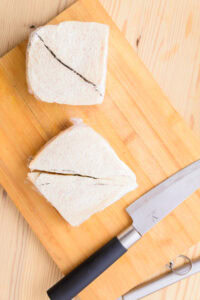 Authentique Fruit Sando - Sandwichs à la fraise: Chauffer brièvement la lame d’un couteau, couper à travers le film en suivant la ligne sans appuyer (petits mouvements d’avant en arrière), essuyer/rincer entre chaque coupe; couper les extrémités, retirer le film, retirer les croûtes si nécessaire, puis couper encore en deux.