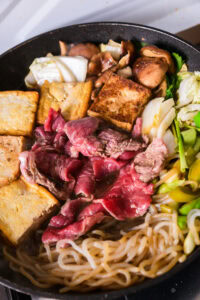 Authentique Sukiyaki - Pousser les ingrédients cuits vers le bord du plat. Ajouter à nouveau du bœuf, cuire une face, puis déposer le bœuf sur les légumes pour l'éloigner du feu direct. Ajouter de la sauce warishita par-dessus et cuire avec l'idée de faire griller dans la sauce plutôt que de faire bouillir.