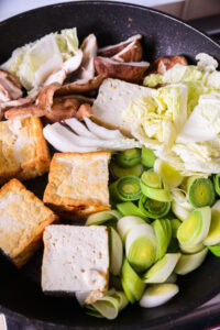 Authentique Sukiyaki - Ajouter les poireaux japonais, le tofu, les shirataki et les autres ingrédients. Ajouter une quantité appropriée de sauce warishita et laisser mijoter jusqu'à ce que les ingrédients s'imprègnent de la sauce. Ne pas rajouter trop vite de sauce quand le tofu rend de l'eau.