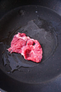 Authentique Sukiyaki - Ajouter une première portion de bœuf, faire dorer une face, ajouter une petite quantité de sauce warishita et laisser le goût pénétrer légèrement. Déguster cette première bouchée.