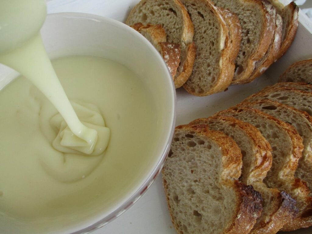 soupe à l'oignon Tranches de pain à côté d’un bol de sauce crémeuse blanche.