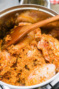 Poulet mariné aux épices dans une casserole, mélangé avec une cuillère en bois.