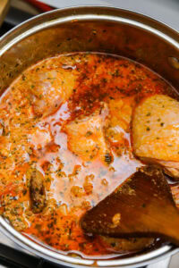 Poulet mijoté dans une sauce tomate épicée, en train de cuire dans une casserole en inox.
