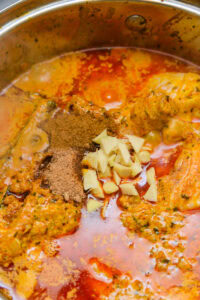 Curry en cuisson dans une casserole avec épices moulues et morceaux de gingembre frais.