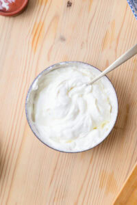Bol de crème fouettée blanche avec une cuillère sur une table en bois clair.