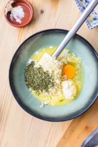 Bol avec œuf, beurre fondu, ail haché et herbes, prêt à être mélangé.