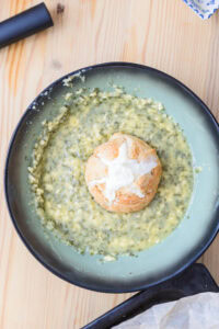 Brioche au centre d’un bol de soupe crémeuse aux herbes, vue de dessus sur table en bois.
